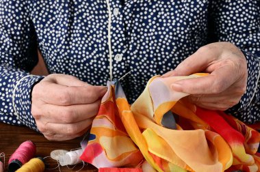 Yaşlı bir kadının elleri dikiş iğnesi tutuyor. Terzinin elleri iş yerinde, yakın plan. Dikiş ve dikiş.