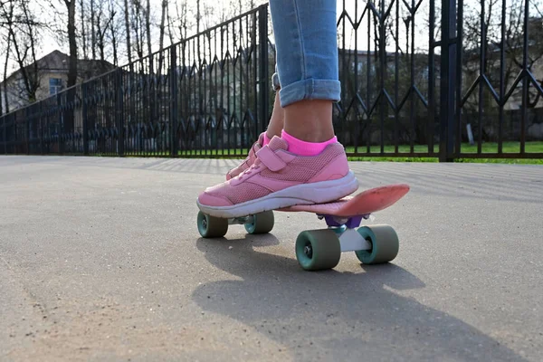 青いジーンズとピンクのスニーカーで女の子のスケートボーダーのクローズアップ足 ピンクのペニースケートロングボードに乗って 国際スケートボードの日 選択的焦点 — ストック写真