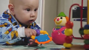 Küçük bir çocuk çıngıraklı yılanlar ve eğitici oyuncaklarla oynar. Bebek yerde tek başına yatıyor ve oynuyor. Bebek gelişiyor.