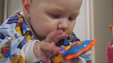 Küçük bir çocuk çıngıraklı yılanlar ve eğitici oyuncaklarla oynar. Bebek yerde tek başına yatıyor ve oynuyor. Bebek gelişiyor.