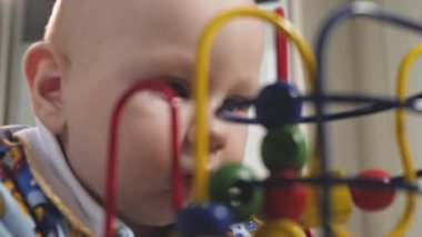Küçük bir çocuk çıngıraklı yılanlar ve eğitici oyuncaklarla oynar. Bebek yerde tek başına yatıyor ve oynuyor. Bebek gelişiyor.