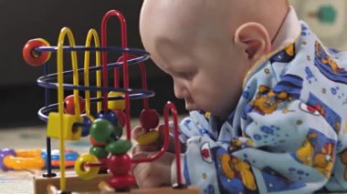 Küçük bir çocuk çıngıraklı yılanlar ve eğitici oyuncaklarla oynar. Bebek yerde tek başına yatıyor ve oynuyor. Bebek gelişiyor.