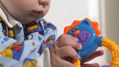 Küçük bir çocuk çıngıraklı yılanlar ve eğitici oyuncaklarla oynar. Bebek yerde tek başına yatıyor ve oynuyor. Bebek gelişiyor.