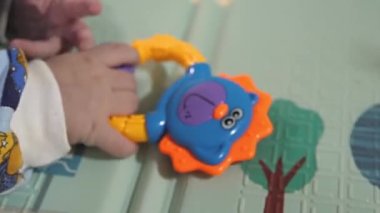 Küçük bir çocuk çıngıraklı yılanlar ve eğitici oyuncaklarla oynar. Bebek yerde tek başına yatıyor ve oynuyor. Bebek gelişiyor.