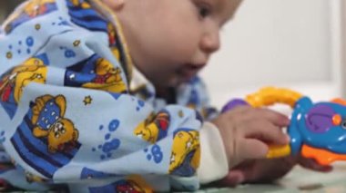 Küçük bir çocuk çıngıraklı yılanlar ve eğitici oyuncaklarla oynar. Bebek yerde tek başına yatıyor ve oynuyor. Bebek gelişiyor.