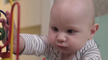 Küçük bir çocuk çıngıraklı yılanlar ve eğitici oyuncaklarla oynar. Bebek yerde tek başına yatıyor ve oynuyor. Bebek gelişiyor.