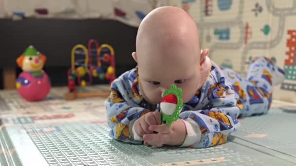 小さな子供がガラガラや教育用のおもちゃで遊んでいます 赤ちゃんは一人で床に横になって遊んでいます — ストック動画