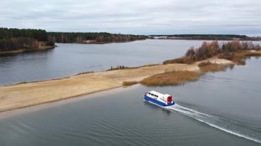 Bir hovercraft bir kum yığınına giriyor ve suya geri dönüyor. Genel plan. İnsanlar ona bakıyor.