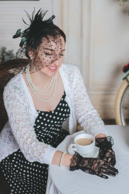 Eski moda giyinmiş genç bir kadın kahve ve kruvasanla sokak kafesinde oturuyor..