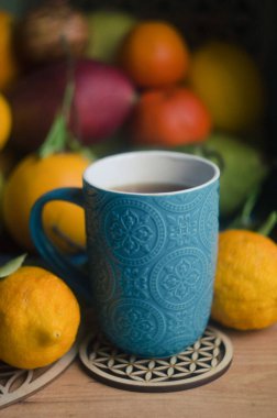 Fruits bergamot, pomegranate, lemon, pamelo, pear, tangerine, mango on a wooden background. Blue ceramic cup with rooibos tea.