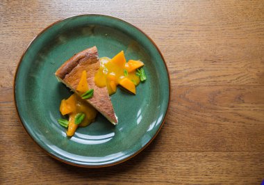 Yeşil tabakta, şeftali dilimleri, nane yaprakları ve ahşap arka planda deniz dikenli karamel kaplı bir parça cheesecake. Kullanışlı tatlıların fotoğrafı.