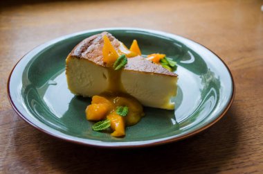 Yeşil tabakta, şeftali dilimleri, nane yaprakları ve ahşap arka planda deniz dikenli karamel kaplı bir parça cheesecake. Kullanışlı tatlıların fotoğrafı.