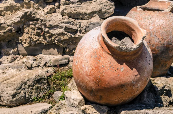 An ancient antique clay jar lies among the ruins of a Mediterranean city. The archaeological value of a photograph of a household item.