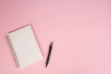 Bir not defteri ve pembe bir yüzey üzerinde bir kalem.