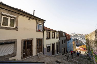 Porto, Portekiz. Mart 2022, şehir merkezinin eski evleri arasında arka planda Dom Louis I demir köprüsü olan nehre doğru giden tipik bir cadde.