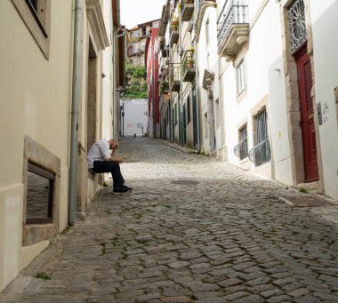Porto, Portekiz. Mart 2022. Şehrin tarihi merkezinde dar bir sokakta evinin basamaklarında bir adam dinleniyor.