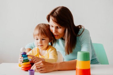 Genç kadın küçük kızıyla oynuyor. Beyaz kadın ve çocuk masada oturup beyaz duvara karşı oynuyorlar..