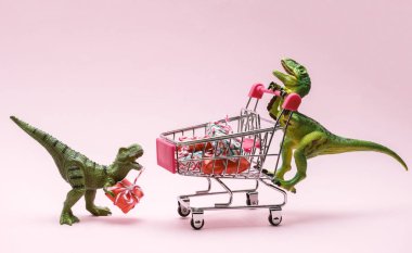 Pembe arka planda hediye kutularıyla dolu alışveriş arabası olan iki sevimli dinozor. Satış konsepti.