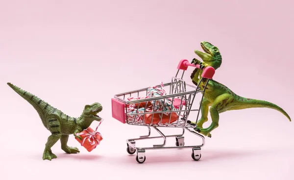 Two cute dinosaurs with shopping trolley full of present boxes on pink background. Sale concept.