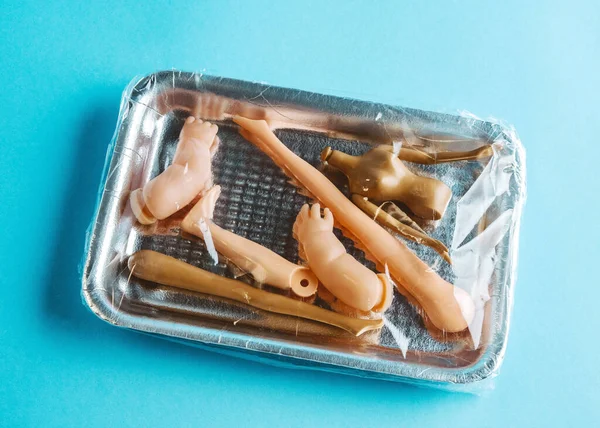 Package covered with food wrap with plastic dolls body parts. Concept of human trafficking and illegal organ trafficking. Conceptual stock photo. Top view on  blue background.