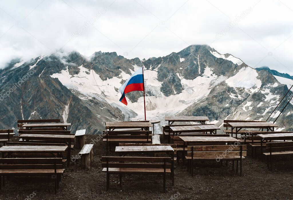 Russian flag waving on a background of mountains covered with snow.