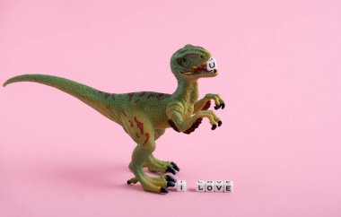 Cute dinosaur and the inscription I love you on a pink background. The dinosaur holds the letter U in its teeth.