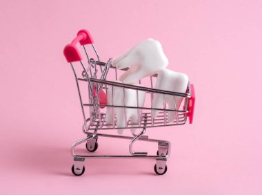 Shopping cart full of teeth on pink background. Investment in dental treatment, discounts at the dental clinic concept.