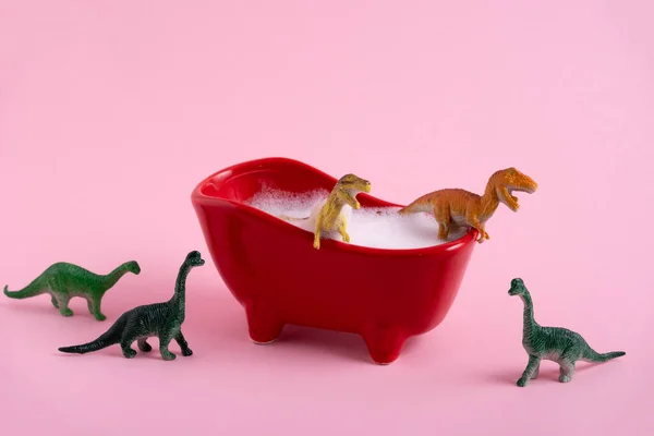 温泉和卫生概念 恐龙在一个粉色背景的满是泡沫的小浴缸里洗澡 — 图库照片