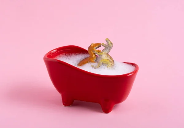 Two dinosaurs take a bubble bath. Bathroom sex humor concept on a pink background.