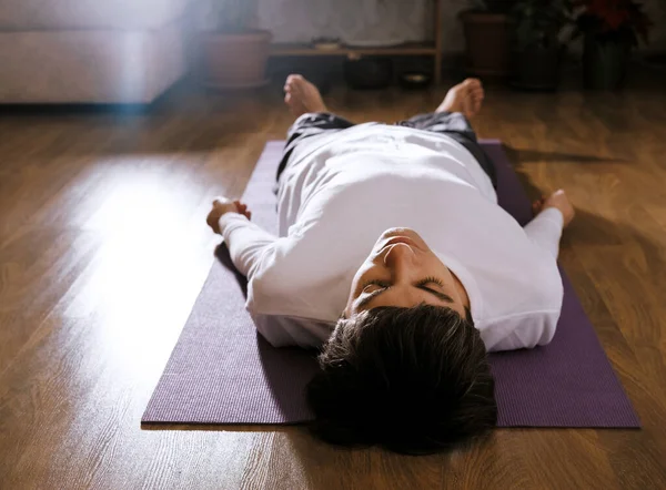 Adam yoga minderinin üzerinde shavasana pozuyla yatıyor. Yoga ve rahatlama kavramı.
