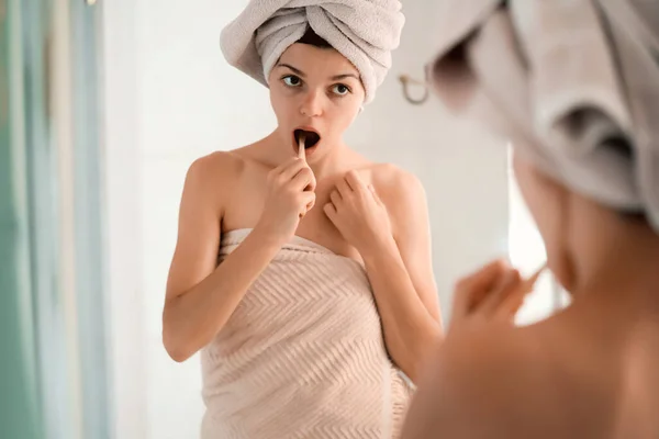 Mujer cepilla sus dientes cerca del espejo. — Foto de Stock