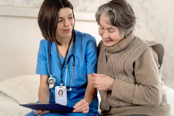 Young nurse is caring for an elderly 80-year-old woman at home, — Stock Photo, Image