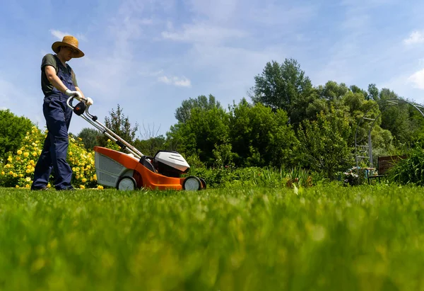Um jardineiro profissional com um cortador de grama cuida da grama no quintal. — Fotografia de Stock