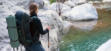 Sırt çantalı ve yürüyüş kıyafetleri içinde yürüyüş direkleri tutan genç bir kız..