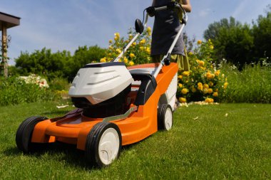 Bir kadın bahçıvan çim biçme makinesiyle çimleri buduyor.