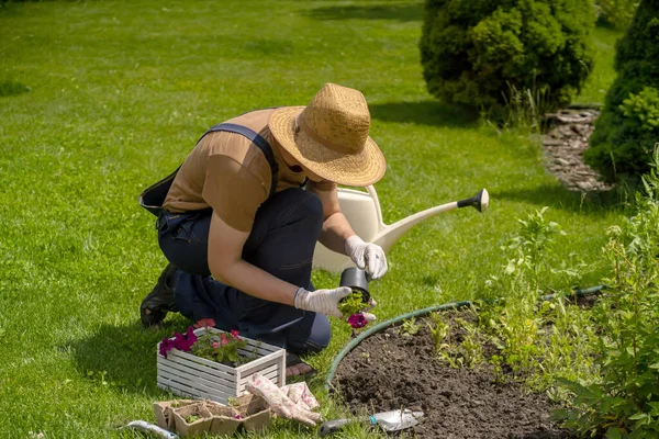 Um jovem em um chapéu de palha e mãos em luvas está envolvido no trabalho de jardinagem., — Fotografia de Stock