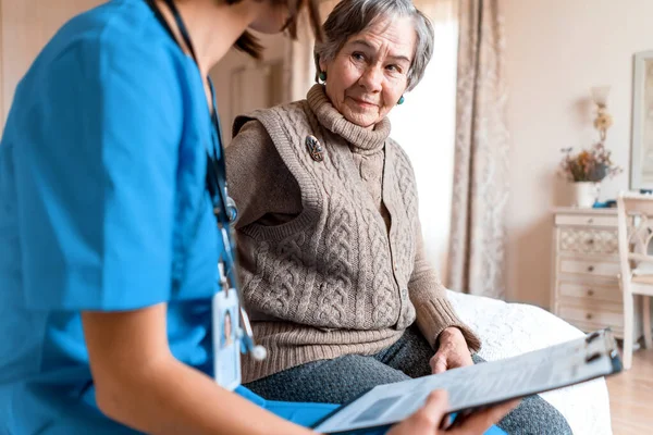 Young nurse is caring for an elderly 80-year-old woman at home, — Stock Photo, Image