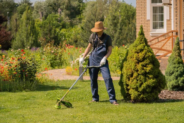 Молодой человек с газонокосилкой заботится о траве на заднем дворе. — стоковое фото