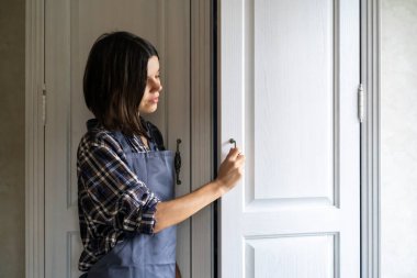 Girl is opening the door of a white wardrobe.