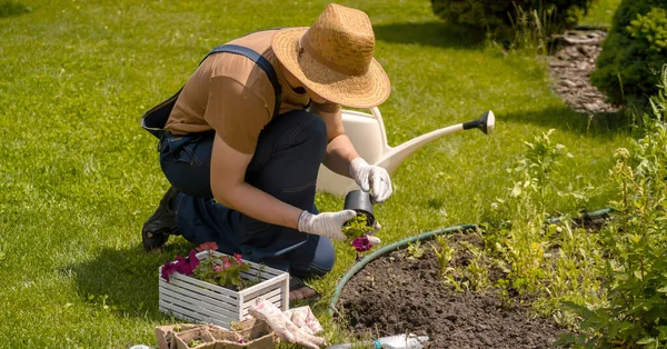 O jovem em um chapéu de palha e mãos em luvas envolve-se no trabalho de jardinagem, — Fotografia de Stock