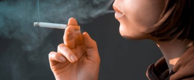 Genç bir güzel kız sigara içiyor, bir kadın stresli ve elinde bir sigara tutuyor, evinin penceresinin yanında duruyor, yakın çekim manzarası var..