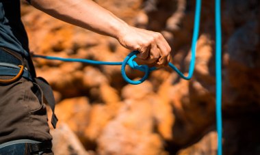 Genç bir adam açık havada dağlara tırmanmaya hazırlanıyor, bir sporcu antrenman sırasında ipe sekiz halat bağlıyor, güneşli bir günde dağcılık, yakın görüş..