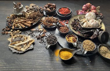 Siyah bir masada çeşitli baharatlar ve otlar.
