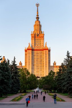 Moskova, Rusya - 17 Eylül 2017: Moskova devlet üniversitesinin ana binası turuncu güneş ışığına dokunuyor ve insanlar gün batımında giriş kapısından parka doğru yürüyorlar.