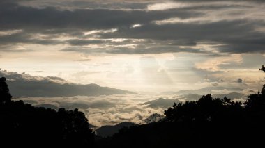 Güneşin bulutlu gökyüzünde, yağmur mevsiminde, ön planda siluetli tropikal orman gibi, dramatik, sakin hava manzarası..