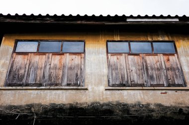 Beton duvarında siyah liken ve yukarıdaki camlarla dekore edilmiş eski ahşap pencereli antik binanın dışı. Çelik alaşımlı, dalgalı bir maddeden yapılmış bir çatı..