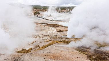 ABD 'nin Wyoming eyaletinin Yellowstone kentindeki Old Faithful bölgesinde turistlerin arka planında bulunan sülfür dumanıyla kaplı sıcak bölge manzarası.