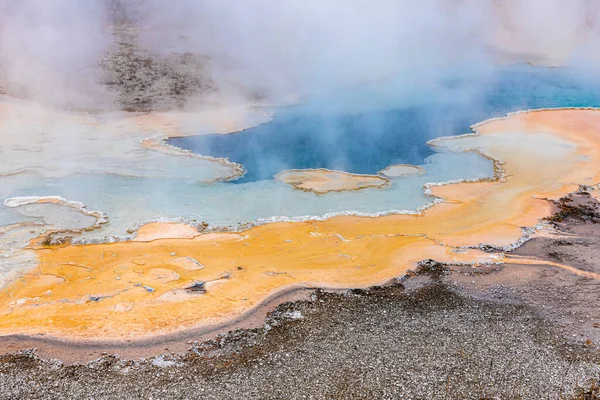 Hot zone of blue and orange minerals in geyser with sulphur smoke inside Yellowstone national park, Wyoming, United states.