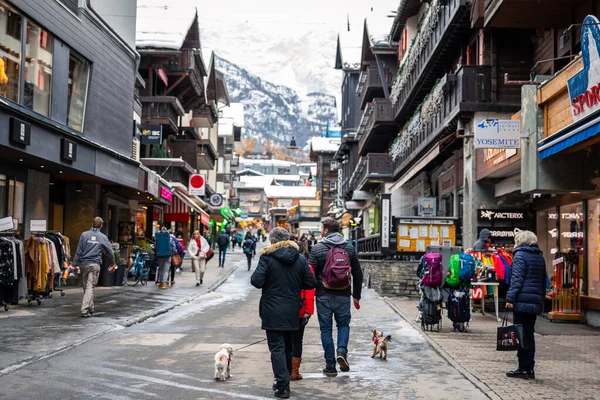 Zermatt, İsviçre - 11 Kasım 2019: Eski kentin içinde köpeklerle birlikte gezen turistler, kış boyunca antik dükkanlar, restoranlar ve alışveriş merkezleriyle çevrelenmiş durumda..