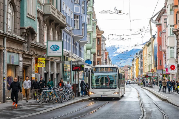 Innsbruck, Avusturya - 3 Kasım 2021: Otoparkın yanındaki duraklarda otobüs durakları bulunan renkli şehir manzarası, yağmur yağdıktan sonra alışveriş ve sokak turları için yürüyüş yapan insanlar. 
